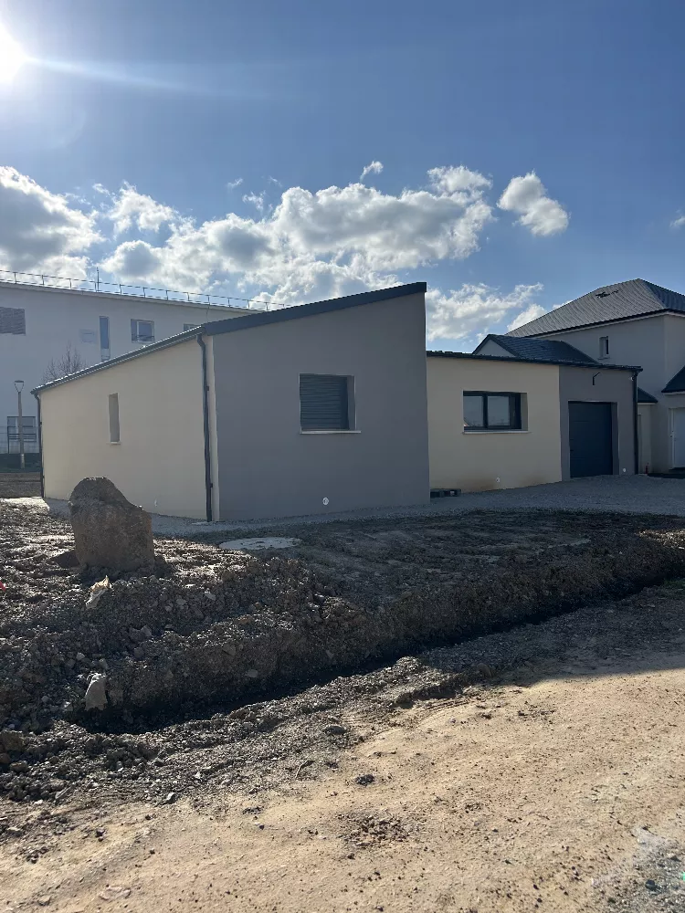 Bâtiment à toit plat et enduit gris, terrain en terre devant