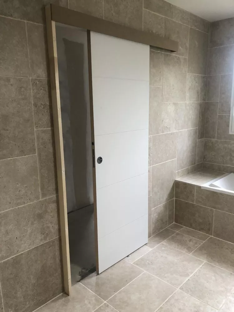 Porte coulissante blanche sur rail apparent dans une salle de bain carrelée